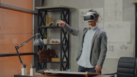 Male-architect-in-office-in-virtual-reality-helmet-uses-gestures-to-manage-a-project-without-leaving-the-office.-Construction-control.-Design-project-of-the-building-and-interior